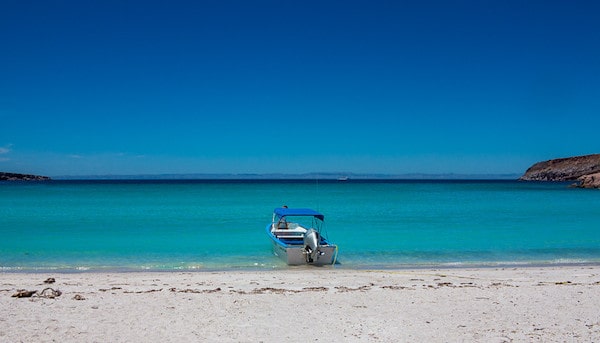 a small boat just on the shore line of a turquoise water beach in Mexico