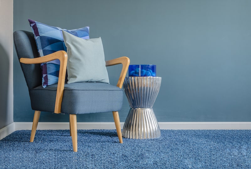 A chair in a corner of a room that has a blue carpet