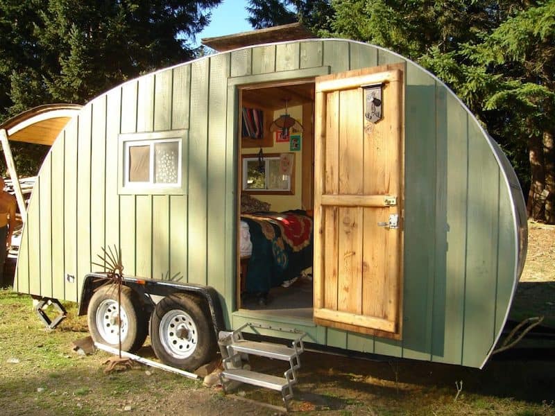 a wooden teardrop trailer painted a natural green color on the outside with the door open and the back hatch open