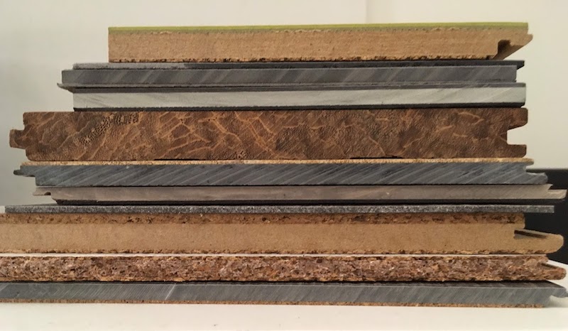 A stack of engineered wood flooring, the top one is marmoleum click where you can see the profile of the fiberboard core, another one is cork on top with a fiberboard core