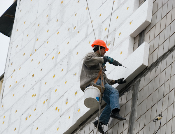EPS insulation being installed on the exterior of a commercial building by a guy being held up by a harness