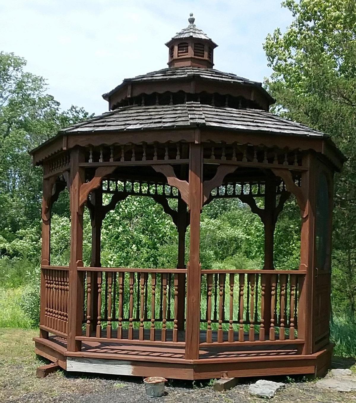 a gazebo in a dark brown color with some New England trees in the background