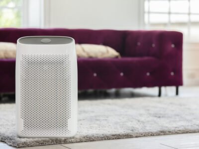 a white rectangle air purifier in a living room, on a rug with a purple couch in the background