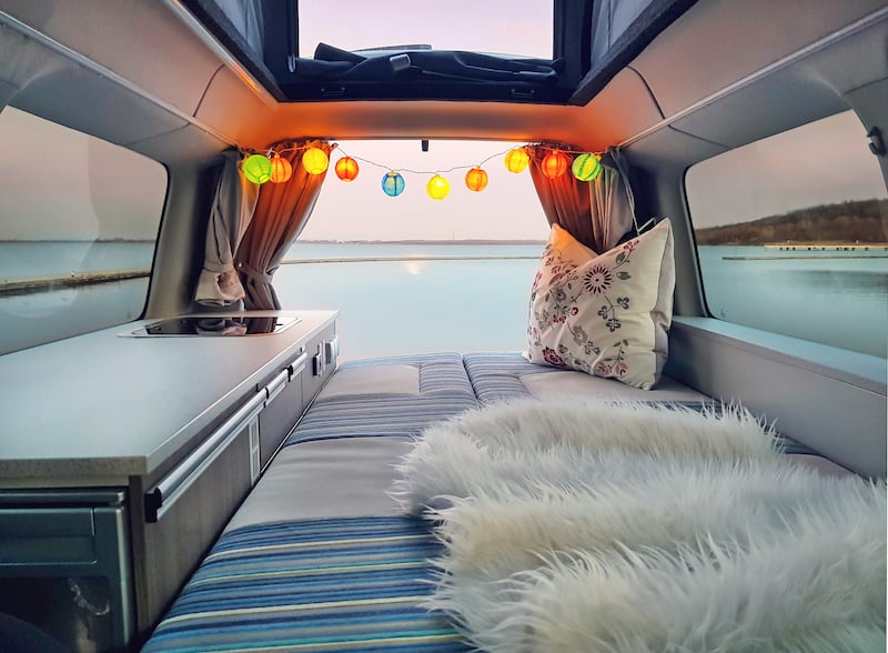 a converted van with the bed folded down looking out to a lake out the back doors